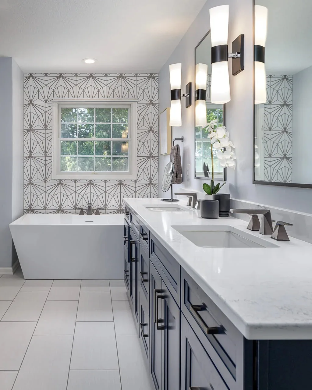 Modern bathroom with tub, vanity, and geometric wallpaper.