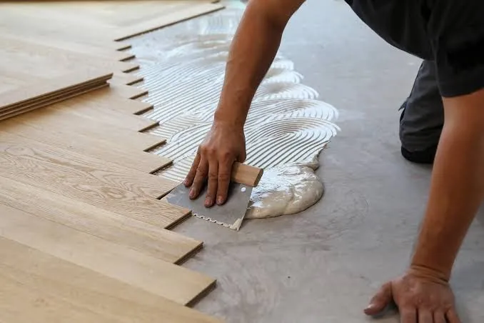Worker applying adhesive for wood flooring installation