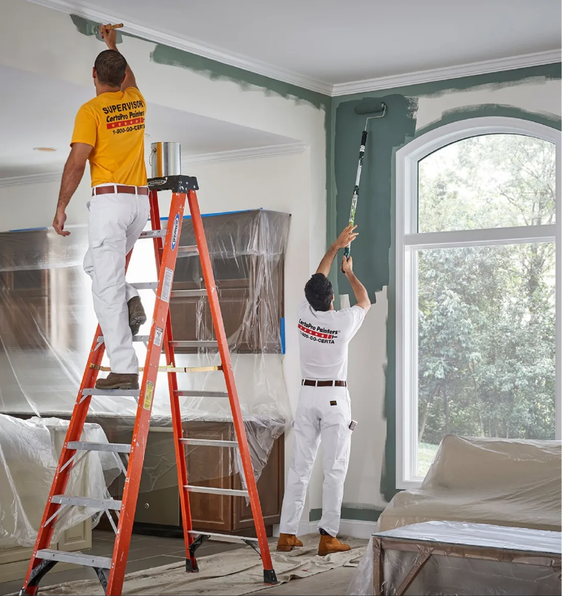 Two painters applying green paint to a living room wall.